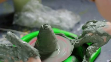 Yedi yaşında, kille kirlenmiş bir çocuk çömlekçi çarkında kilden bir ürün yapmaya konsantre oluyor. Yakın plan. Yatay.