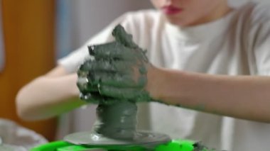 Yedi yaşında, kille kirlenmiş bir çocuk çömlekçi çarkında kilden bir ürün yapmaya konsantre oluyor. Yakın plan. Yatay.