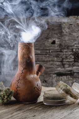Eski kahverengi buhar bongu ve açık kenevir öğütücüsü ile doğranmış marihuana otu ve tıbbi kenevir tomurcuğu ahşap tüy ve çuval bezi ile duman içinde. Dikey yönelim