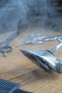 Ahşap bir yüzeyde eski berber aletleri vardır. Klasik manuel saç makasi, tarak, dumanin içinde kuaför makasi. Yakın plan. Berber dükkanı geçmişi. düşey yönelim.