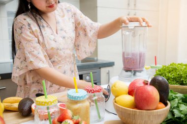 Mutlu kadın taze sıkılmış meyve ve sebze hazırlarken mutfakta kahvaltıda meyve püresi yapmayı seviyor. Diyet ve sağlık konsepti..