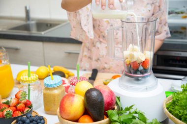 Mutlu kadın taze sıkılmış meyve ve sebze hazırlarken mutfakta kahvaltıda meyve püresi yapmayı seviyor. Diyet ve sağlık konsepti..