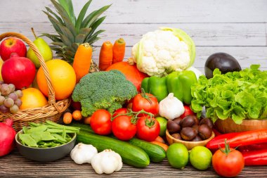 Toplu sebzeler ve meyveler, üzümler, portakallar, ananaslar, ahşap sepetteki muzlar, havuçlar, domatesler, guava, biber, patlıcan, altın kapsül, ahşap masada yeşil salata..