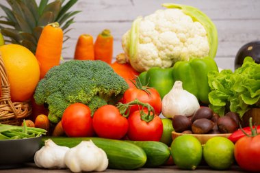 Toplu sebzeler ve meyveler, üzümler, portakallar, ananaslar, ahşap sepetteki muzlar, havuçlar, domatesler, guava, biber, patlıcan, altın kapsül, ahşap masada yeşil salata..