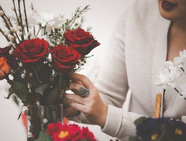 Çevrimiçi ev çiçekleri düzenleme konsepti, kırmızı ve pembe gülleri budamaya hazırlanan kadın ve evdeki güzel çiçek düzenlemeleri, Sevgililer Günü için hediye olarak vazo ile çiçek düzenlemeleri. 