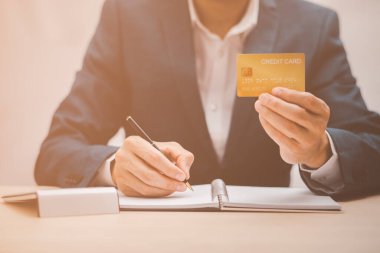 İşadamı, kredi kartı, kredi kartı, dizüstü bilgisayar, çevrimiçi alışveriş konsepti, bankacılık ve çevrimiçi ev alışverişi gibi finansal işlemler içeren kağıtlara el yazısı yazar..