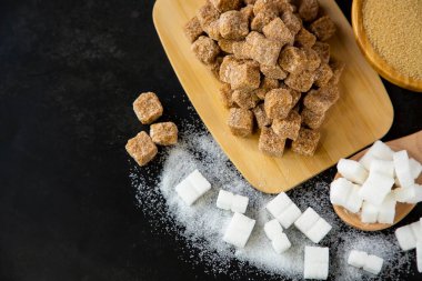 Koyu arkaplanda bir kase ahşap, beyaz ve kahverengi kum şekeri ve şeker.