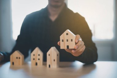 Mini ahşap ev modelini ahşap masadan seçen, emlak almayı planlayan, emlak almayı planlayan bir adam. En iyisini seç konsepti.
