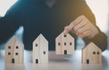 Mini ahşap ev modelini ahşap masadan seçen, emlak almayı planlayan, emlak almayı planlayan bir adam. En iyisini seç konsepti.