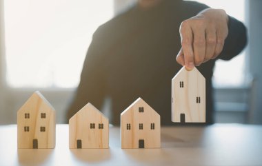 Mini ahşap ev modelini ahşap masadan seçen, emlak almayı planlayan, emlak almayı planlayan bir adam. En iyisini seç konsepti.