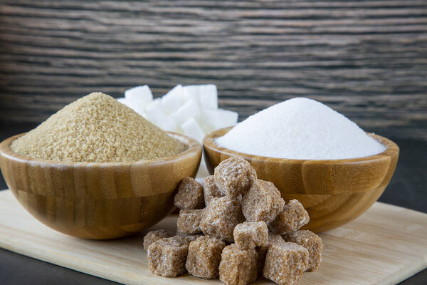 Древесина миски и белый и коричневый песок сахар и комок сахара на темном фоне