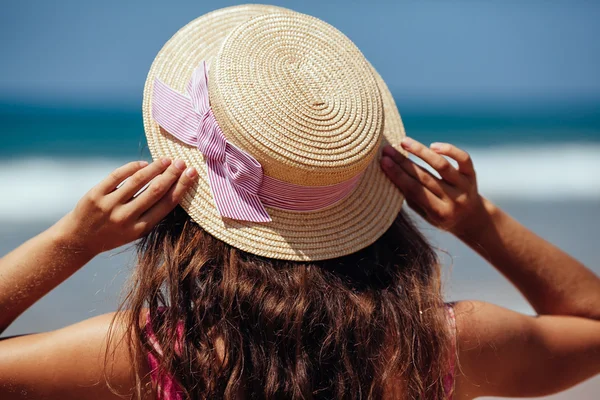 Jovem mulher de pé em uma praia segurando seu chapéu de palha e olhar — Fotografia de Stock