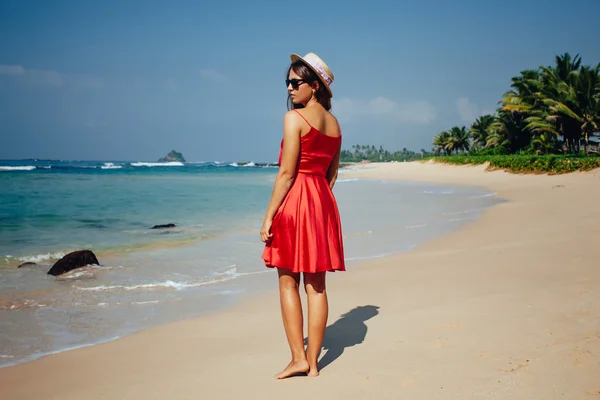 Happy woman enjoying beach relaxing joyful in summer by tropical blue water. Beautiful red dress model happy on travel wearing beach sun straw hat on sandy beach — Stock Photo, Image