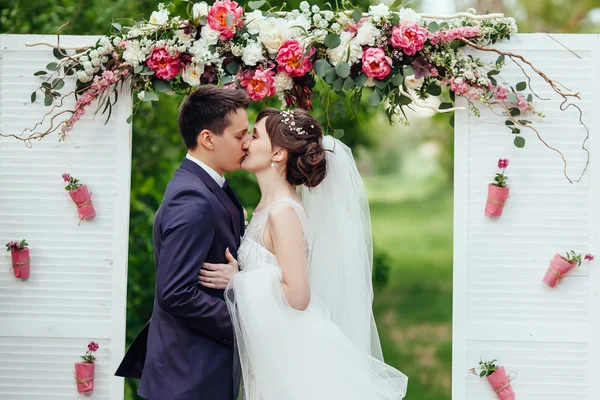 Noiva elegante e noivo beijo no fundo flor casamento ar — Fotografia de Stock