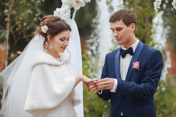 Pengantin pria dan wanita bergaya saling bertukar cincin di flo latar belakang — Stok Foto
