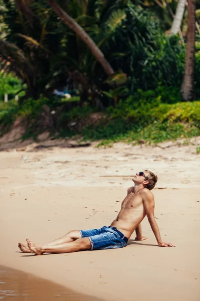 Homme relaxant sur une plage tropicale. Jeune homme bronzé prenant sunbat — Photo