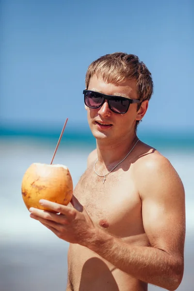 attractive man drinks coconut juice from a nut on a beach at the