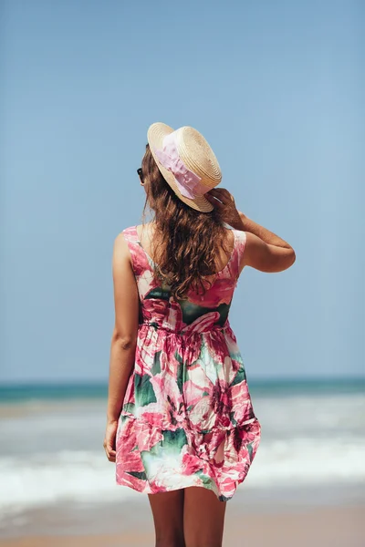 Giovane donna in piedi su una spiaggia che tiene il cappello di paglia e cerca — Foto Stock