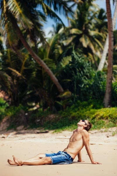 Man relaxing on a tropical beach. Young tanned man taking sunbat