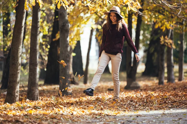 Outono / queda mulher feliz jogando folhas para cima no ar com perna — Fotografia de Stock