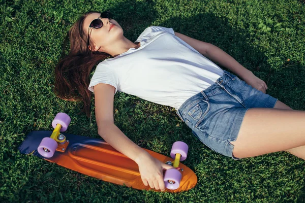 Teenie-Mädchen, das mit seinem Skateboard auf Gras ruht. hübscher Teenager — Stockfoto