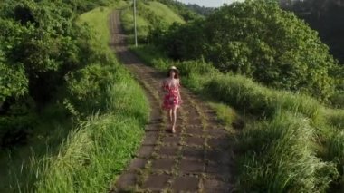 Campuhan Tepesi 'nde yürüyen kırmızı elbiseli genç bir kadının insansız hava aracı görüntüsü, Bali' de yeşillik yolu, Ubud
