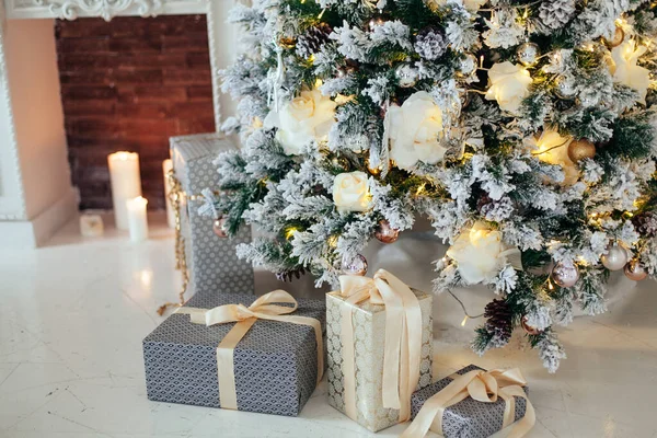 Pilhas de presentes de Natal em papel branco e cinza sob uma árvore de Natal decorado bolas brancas e douradas perto de lareira na sala de estar. — Fotografia de Stock