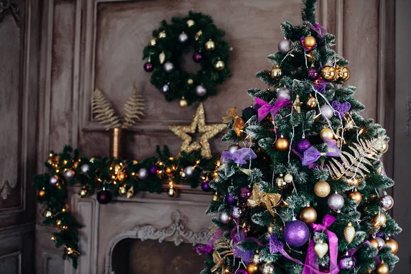 Рождественские и новогодние украшения роскошный интерьер комнаты с подарками и новогодняя елка возле камина и диван в фиолетовых и золотых тонах Стоковое Изображение