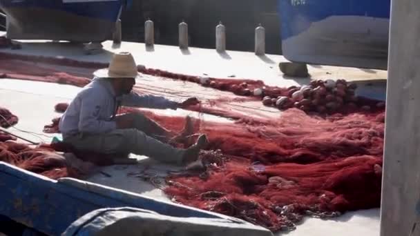 Maroko, Essaouira - październik 2019: Rozplątanie sieci, rybacy w kapeluszu zaciągający i naprawiający tradycyjne czerwone sieci rybackie siedząc ręcznie na molo — Wideo stockowe