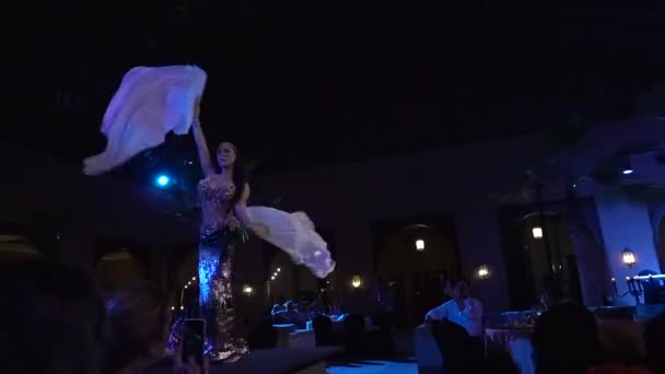 Marokko, Marrakesch - Oktober 2019: Traditionelle orientalische Bauchtänzerin arabische Frau tanzt in hell glitzerndem Kleid mit weißen Tüchern in den Händen auf der Bühne vor dem Publikum. — Stockvideo