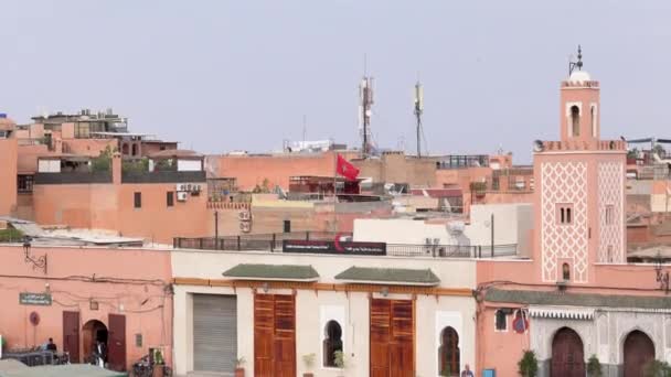 Marruecos, Marrakech - Octubre 2019: Vista panorámica del exterior del edificio árabe local con la bandera nacional marroquí ondeando afuera, símbolo del país sobre el horizonte panorámico de la ciudad en un día soleado — Vídeos de Stock