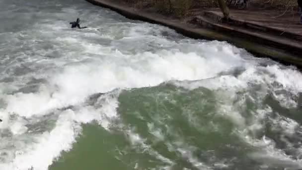MUNICH, GERMANY - 2020 Mart: Siyah dalış takımlı profesyonel sörfçü Eisbach Nehri 'nde kış boyunca İngiliz Bahçesi' nde sörf yapıyor — Stok video