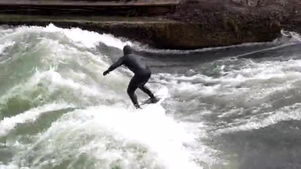 MUNICH, GERMANY - MARCH 2020: Professional surfer man in black diving suit surfing On Eisbach River, Englischer Garden during winter — Stock Video