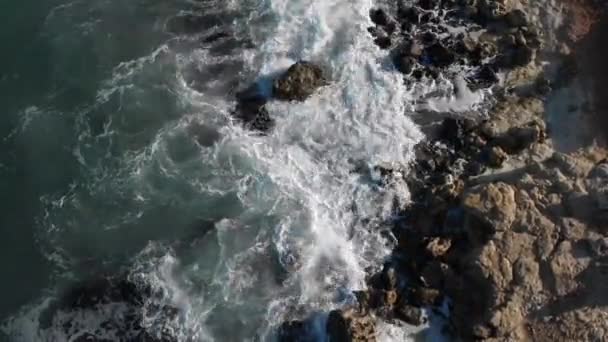 Pájaros vista de las olas del océano estrellándose contra la playa de roca desde arriba. Las olas de vista superior se rompen sobre piedras vacías en un océano azul. Vista aérea del dron de las olas del mar 4k tiro — Vídeo de stock
