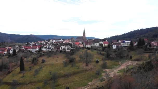 Letecký pohled na městečko s budovami s kachlovými střechami mezi horami a kostelem uprostřed v jarním slunném dni. Krásné drone video nad malou bavorskou vesnicí na venkově v Německu — Stock video
