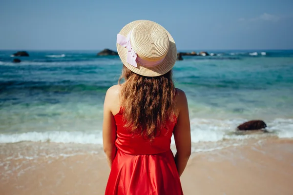 Mulher bonita elegante em vestido vermelho e chapéu de palha na praia . — Fotografia de Stock