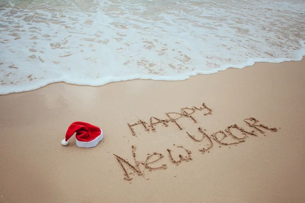 Happy new year written in the sand with santa hat — Stock Photo, Image