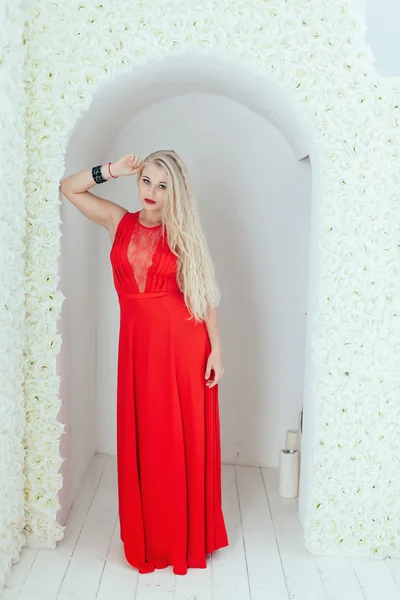 Красивая блондинка с красными губами в красном платье позируя в цветок — стоковое фото