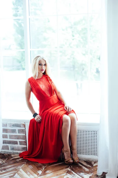 Молодая сексуальная блондинка с красными губами в красном платье позирует в интерьере — стоковое фото
