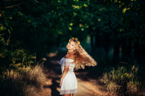 Porträtt av blond flicka klädd i vit klänning med blomma krans — Stockfoto