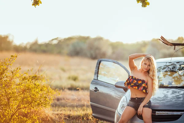 Счастливая молодая женщина с автомобилем - сексуальная богатая женщина-водитель с длинными светлыми волосами — стоковое фото