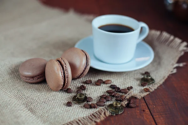Chocolate macaroons,beans and coffee in mug on wooden table back — Stock Photo, Image