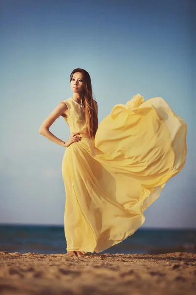 Beautiful fashionable model on the beach in yellow long dress — Stock Photo, Image