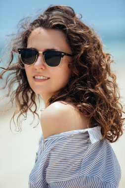 Güneş gözlüğü ve çizgili gömlekli deniz ve gökyüzü arka plan üzerinde poz güzel gülümseyen kız. Moda portraite kadının tropikal plaj