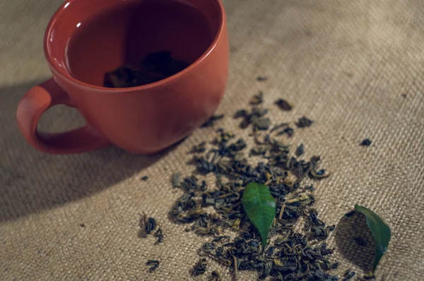 Té seco con hojas verdes en taza, sobre fondo de arpillera —  Fotos de Stock