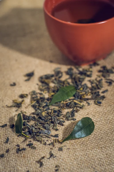 Kuru çay Kupası, çuval bezi zemin üzerine yeşil yaprakları ile — Stok fotoğraf
