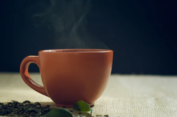 Dry tea with green leaves in cup, on burlap background — Stock Photo, Image