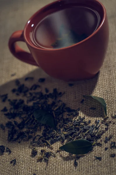 Сухий чай з зеленим листям в чашці, на тлі мішковини — стокове фото
