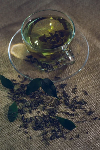 Té seco con hojas verdes en taza, sobre fondo de arpillera —  Fotos de Stock