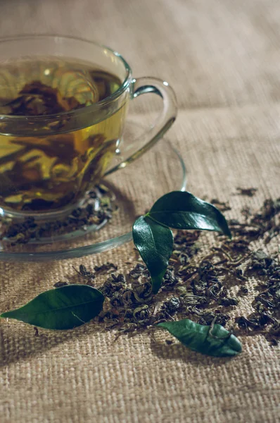 Té seco con hojas verdes en taza, sobre fondo de arpillera — Foto de Stock